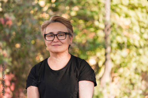 Pensive, sad Asian woman in a black T-shirt in the park, a little gray hair, sunny day in autumn, space for text