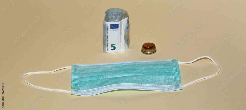plain surgical mask, banknote of 5 euro and few coins partly in soft focus close up isolated on pastel color background, concept of high price of medical products plain surgical mask, banknote of 5 euro and few coins partly in soft focus close up isolated on pastel color background, concept of high price of medical products