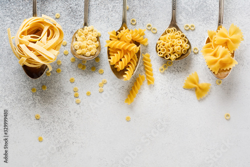 Various pasta in iron spoons on gray concrete background. Anellini pasta. Cooking concept. Top view.