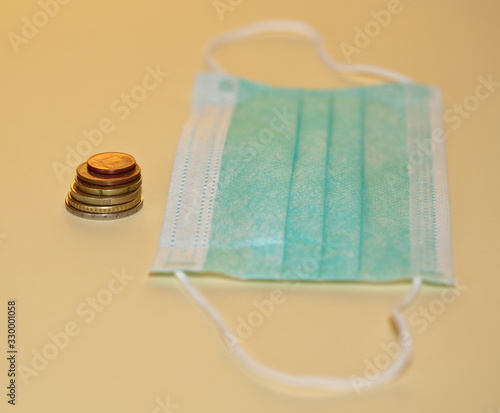 Coins and sanitary / hygienic face mask close up isolated on pastel color background photo