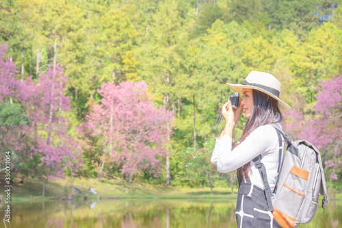 Smiling woman traveler in pink sakura blossom park at doi inthanon landmark chiang mai thailand with backpack arms raised and enjoying view of nature on holiday, relaxation concept, travel concept