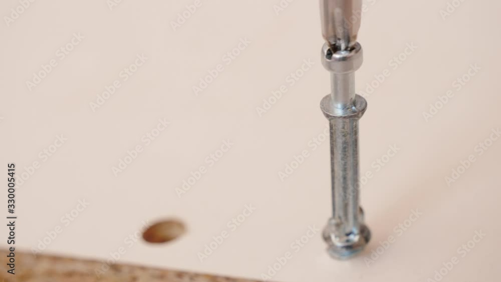 Assembling furniture at home. Mounting screw is screwed into hole board. Closeup of tool in hand. Do it yourself furniture assembly Assembling furniture at home. Mounting screw is screwed into hole board. Closeup of tool in hand. Do it yourself furniture assembly