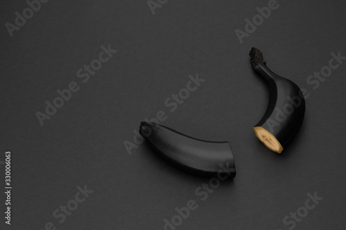 Two halves of a black banana on the matte black background. Minimal style. Conceptual minimalist black art. Matte surface. Cut fruit. One. Space for text