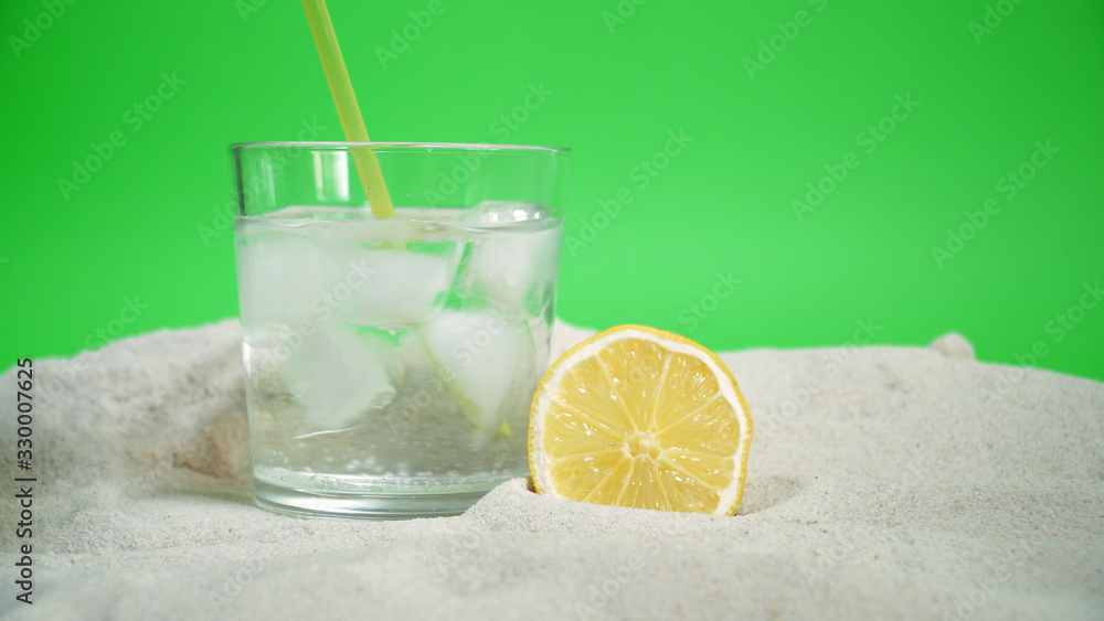 Fototapeta premium glass with ice and soda water and lemon on the sand on a green background