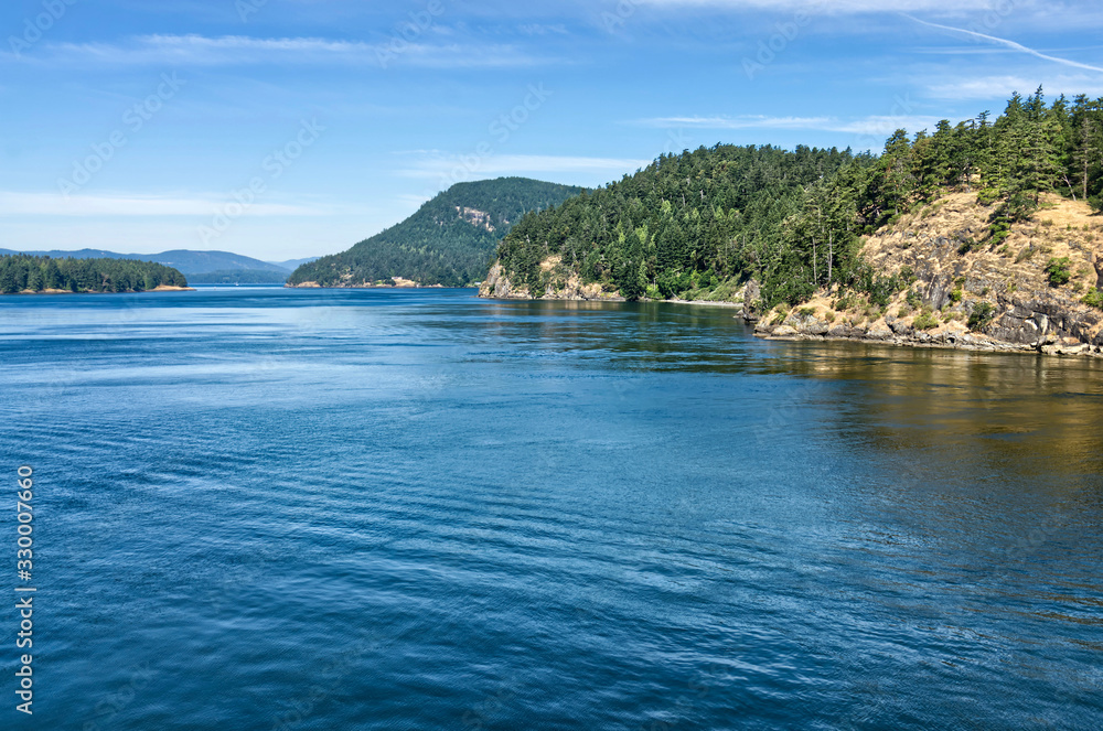 beautiful Southern Gulf Islands in the Strait of Georgia from the ferry. Islands with evergreen conifers and turquoise sea water on a bright sunny day. Trip from Vancouver to Victoria, Canada