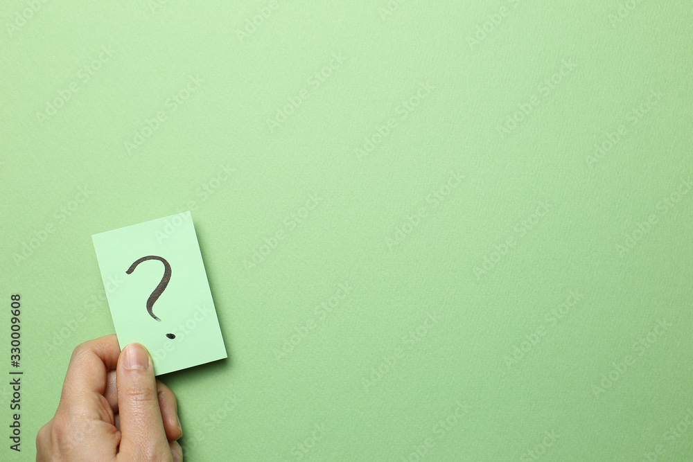 Hand holding question mark memo paper on green background. Solution concept Hand holding question mark memo paper on green background. Solution concept