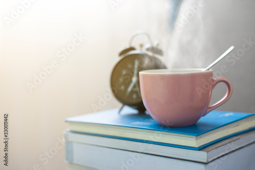 Hot coffee put on many book or notebook and front of alarm clock near curtain that all is on interior furniture or sofa in soft light ray background of window,this image in lifestyle or coffee concept