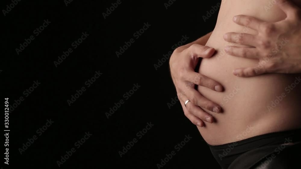 The figure of a pregnant girl on a black isolated background in the studio. Hands gently touch the abdomen. The figure of a pregnant girl on a black isolated background in the studio. Hands gently touch the abdomen.
