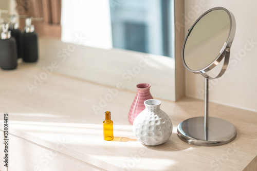 Obraz na plátně Dressing table with circle mirror, small flower vase in glossy ceramic white and pink vase and reagent bottle on the wooden counter for everyday skin care and cosmetic