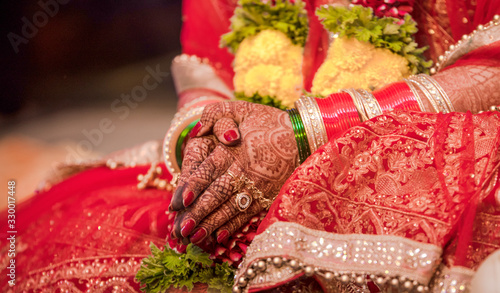 Photography Beautiful photo of Indian bride in traditional wedding attire as per Hindu custom, wearing colorful bangles in hands decorated with henna mehndi is sitting with folded hands in her marriage ceremony