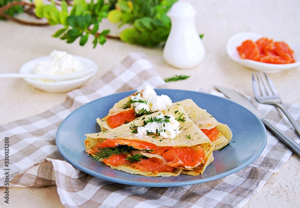 Thin crepe pancakes with salted salmon and cream cheese on a gray plate on a light concrete background. French cuisine. Pancake Day. Thin crepe pancakes with salted salmon and cream cheese on a gray plate on a light concrete background. French cuisine. Pancake Day.