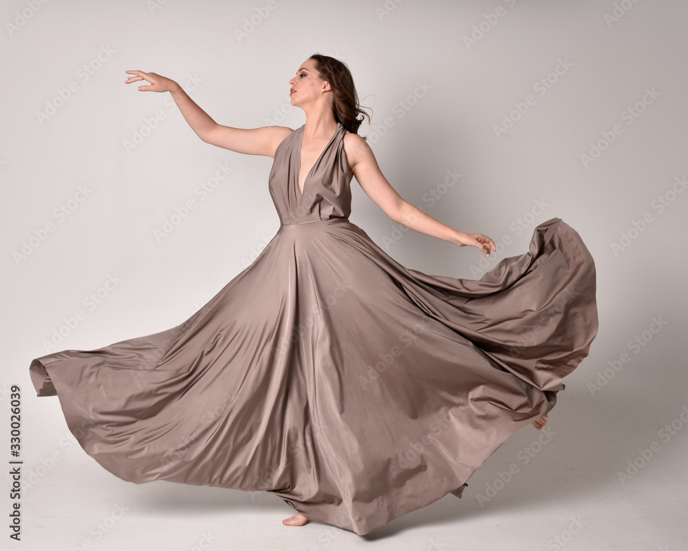 Portrait of a pretty brunette girl wearing a long silver evening gown, full length standing pose against a studio background. Portrait of a pretty brunette girl wearing a long silver evening gown, full length standing pose against a studio background.