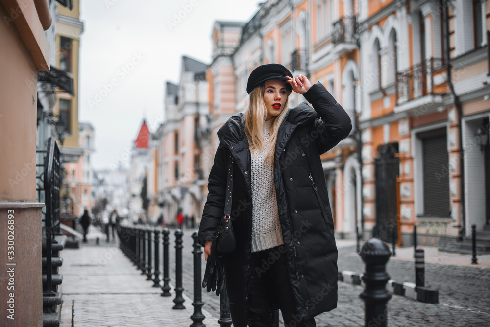 Young beautiful girl in stylish hat and with a fashionable coat near vintage street in european city