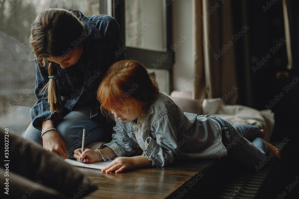 Beautiful girl with little sister. Family sitting in the room near window Beautiful girl with little sister. Family sitting in the room near window