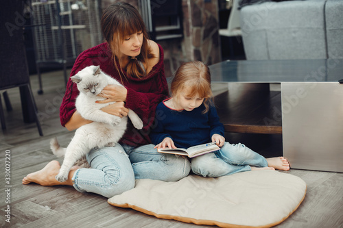 Beautiful mother with little daughter. Family sitting in the room. Cute girl doing homework. Woman playing with kitty photo