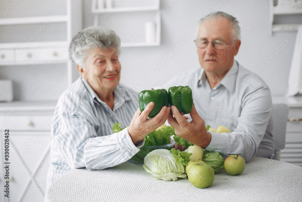 Couple in a kitchen. Grandparents sitting at home. Woman with vegetables Couple in a kitchen. Grandparents sitting at home. Woman with vegetables