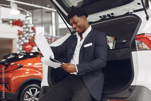 Man buying the car. Businessman in a car salon. Black male in a suit. © prostooleh