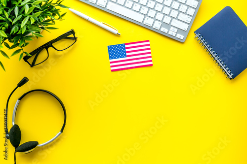 Learn English online. Concept with American - USA - flag, headset and keyboard on yellow background top-down copy space