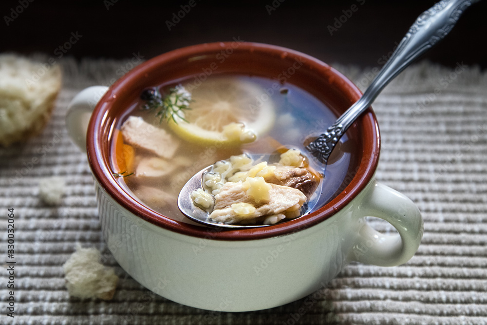Delicious homemade chicken broth soup with lemon slice. Noodle soup in bowl and breadcrumbs on table napkin.