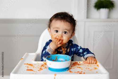 Baby eating carrot puree with his fingers
