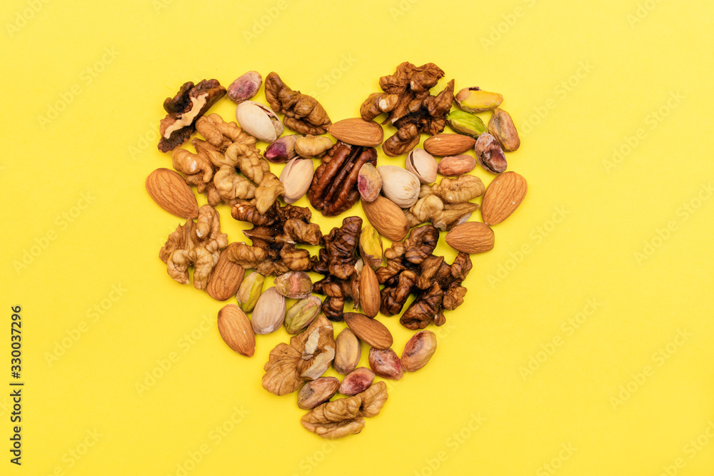 Obraz premium Flat lay ketogenic diet. Walnut,pistachios,pecan,almond are laid out in the form of heart on the yellow background. Concept of healthy food.