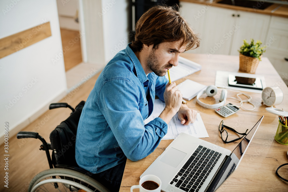 Pensive businessman in wheelchair using laptop while working at home.
