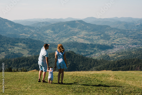 Mom  dad and daughter in the mountains enjoy and look at nature. Back view. Young family spending time together on vacation  outdoors. The concept of family summer holiday.