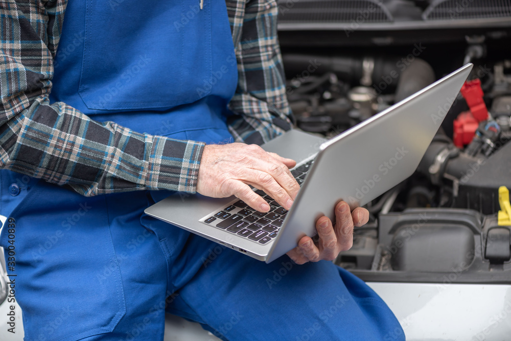 Mechanic using laptop for checking car engine
