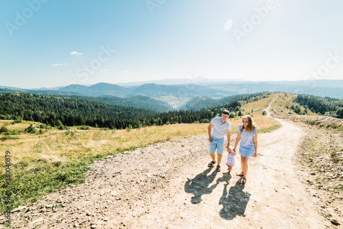 Portrait of happy family. Mom, dad and daughter walk in mountains in nature. Young family spending time together on vacation, outdoors. The concept of summer holiday. Mother's, father's, baby's day.