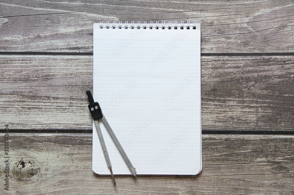 Notepad with a blank white sheet in a checker paper with compass lies on the background of wooden boards Notepad with a blank white sheet in a checker paper with compass lies on the background of wooden boards