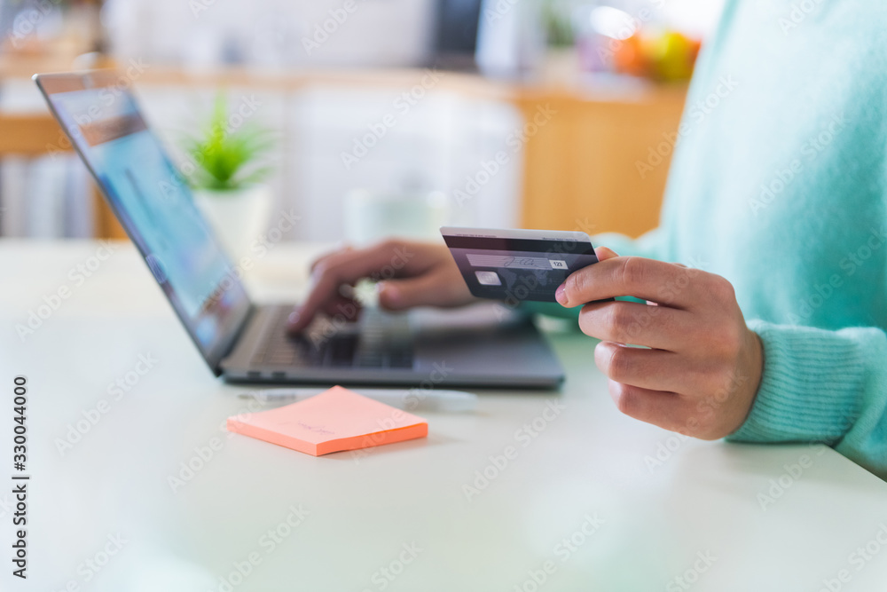 Close up of female hands holding a credit card and making a purchase using a laptop Close up of female hands holding a credit card and making a purchase using a laptop
