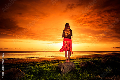 Frau mit rotem Kleid bei Sonnenuntergang am Meer