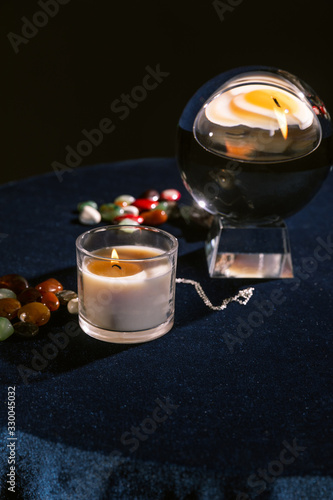Selective focus of crystal ball, candle, fortune telling stones on dark blue velour fabric isolated on black