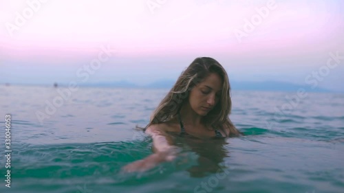 Beautiful slim and young girl swims in the turquoise sea. Long hair and a slender figure in the model. A woman dives under water and splashes. The concept of calm, happiness and relaxation.