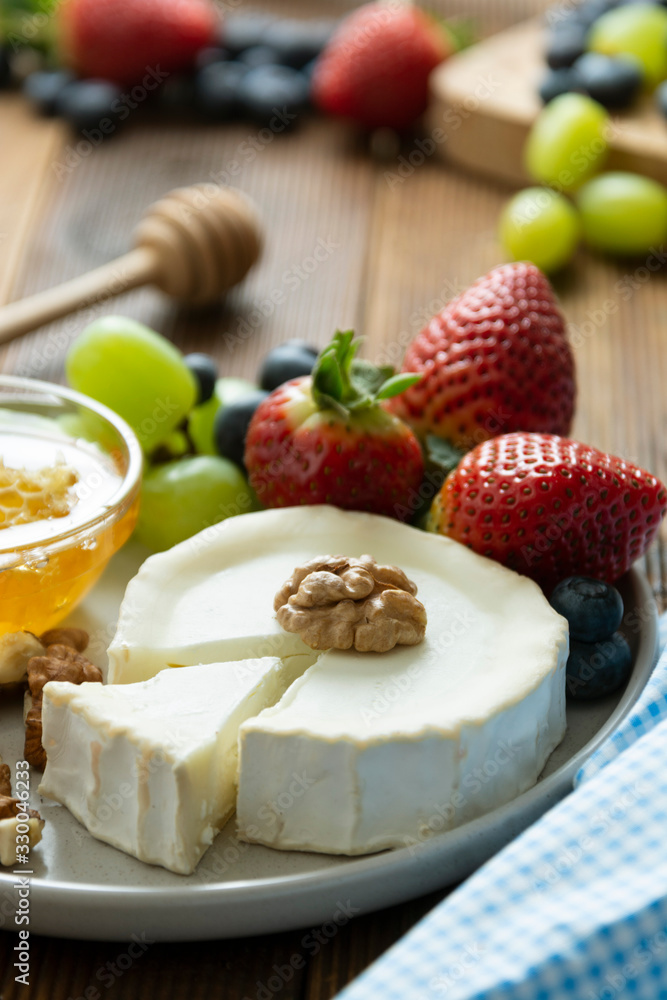 Cheese plate round sliced soft cheese, blueberry, strawberry, grapes and honey on wooden table. Cheese plate round sliced soft cheese, blueberry, strawberry, grapes and honey on wooden table.