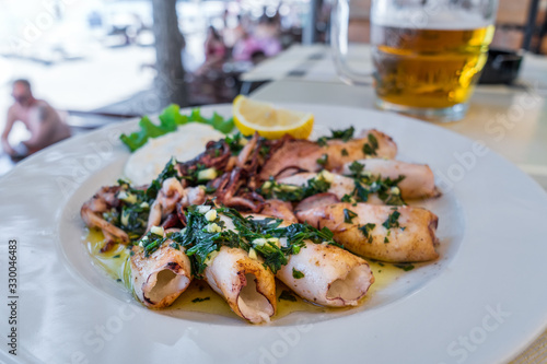 Grilled squids with herbs  garlic and lemon on white plate close-up. Popular and delicious Mediterranean meal.