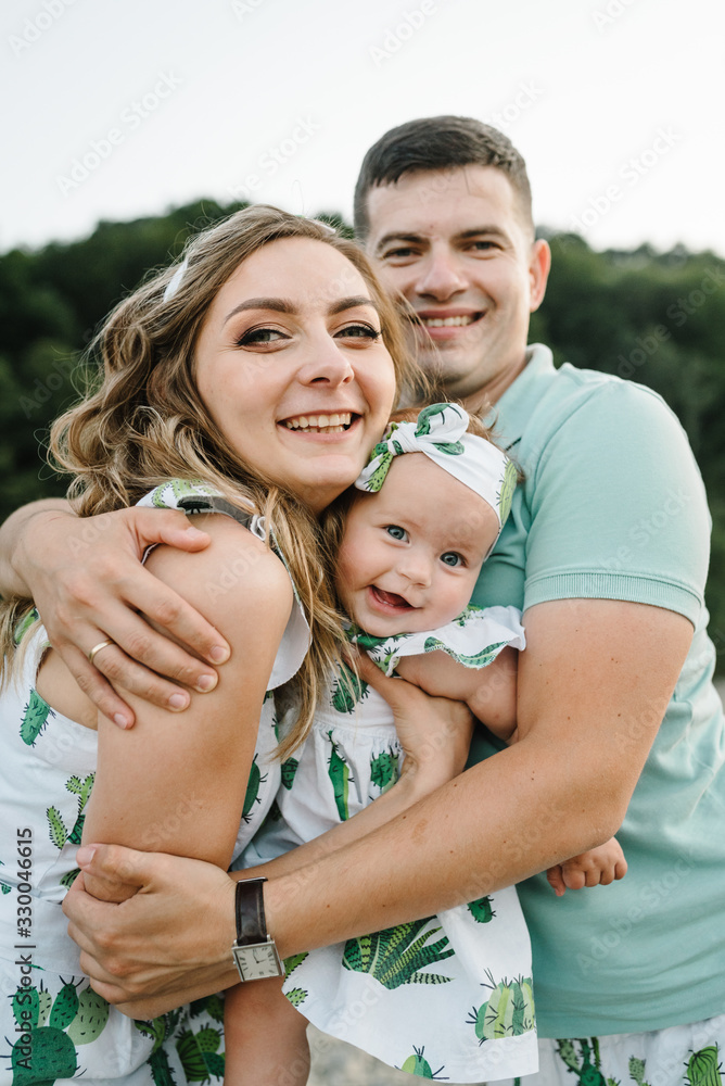 Fototapeta premium Mom, dad and daughter hugging, enjoy and walking at nature. Young family spending time together on vacation, outdoors. The concept of summer holiday. Family look.