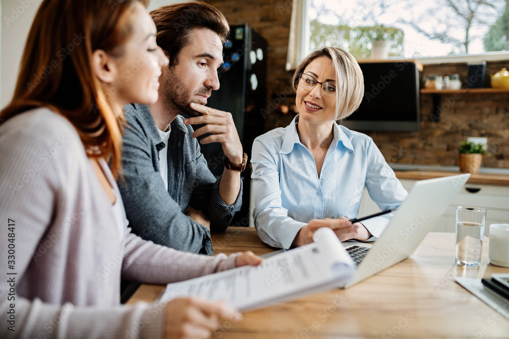 Smiling financial advisor using laptop while having a meeting with young couple. Smiling financial advisor using laptop while having a meeting with young couple.