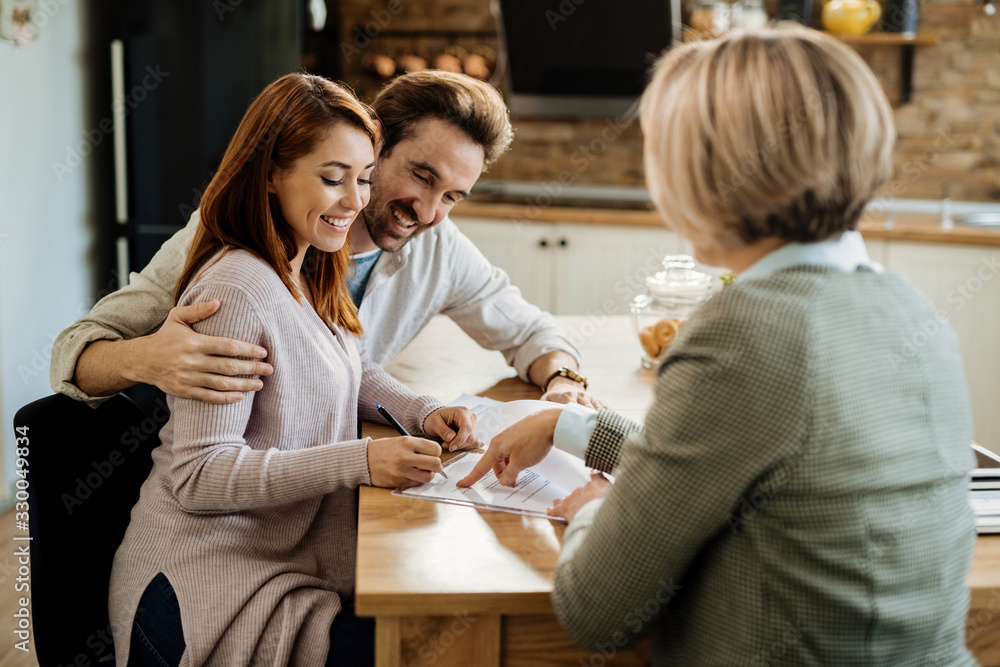 Happy woman and her husband signing an agreement with insurance agent.
