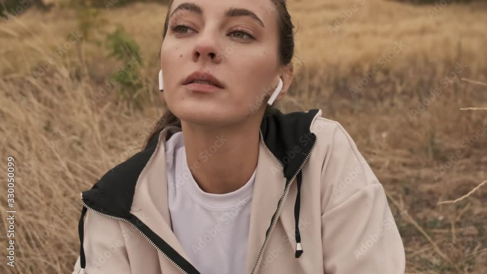 Pleased pretty athletic woman in earphones relaxing after training at seashore Pleased pretty athletic woman in earphones relaxing after training at seashore