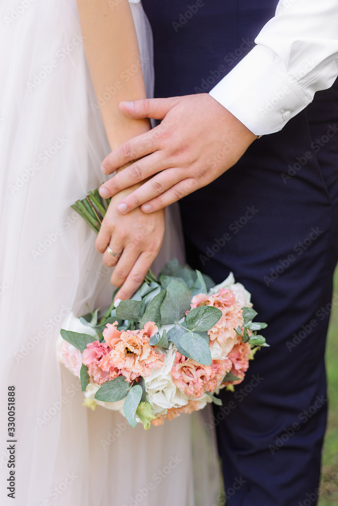 The groom holds the hand of the bride. She has in her hand a tender light wedding bouquet. The groom holds the hand of the bride. She has in her hand a tender light wedding bouquet.