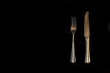 Minimalism on a black background. Two golden table cutlery. Abstraction and creativity.