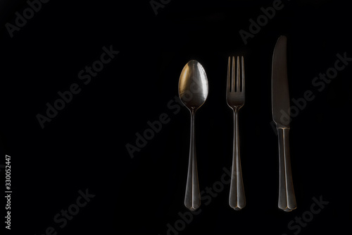 Minimalism on a black background. Three golden table cutlery. Abstraction and creativity.