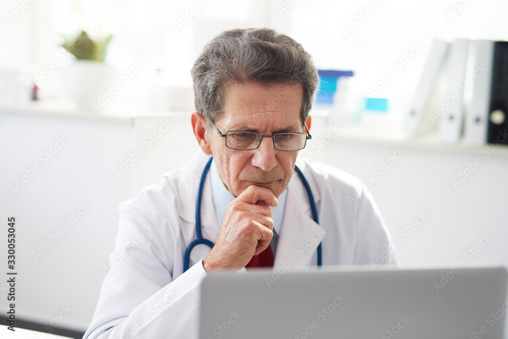 Senior doctor working with a laptop in doctor’s office Senior doctor working with a laptop in doctor’s office