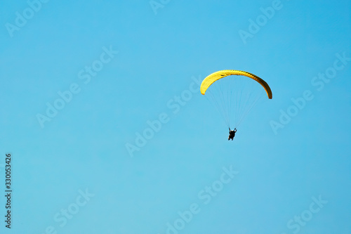 Brave paraglider glides through the blue sky on a parachute in the wind. Extreme sports and outdoor activities