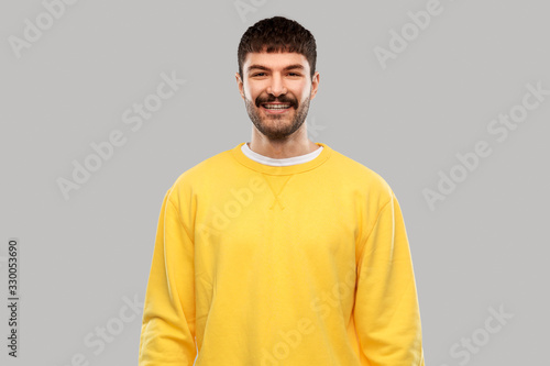 people concept - smiling young man in yellow sweatshirt over grey background