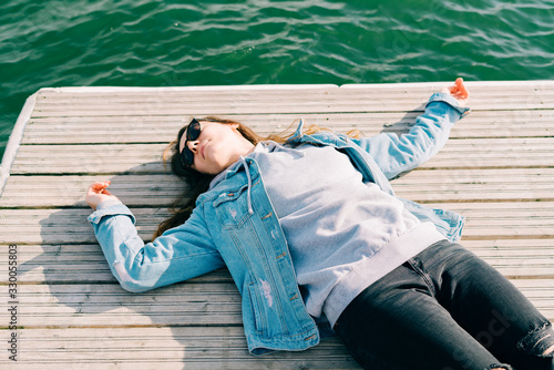 a young pretty girl in a denim jacket and glasses is lying on a pier near the lake on a Sunny spring day photo