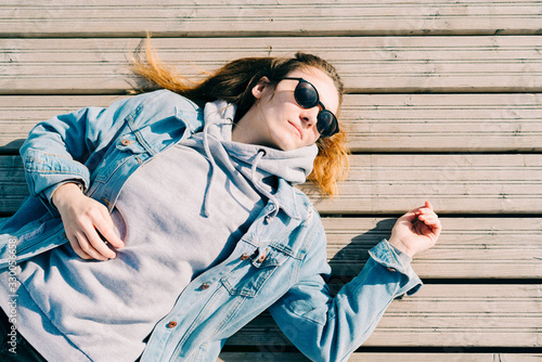 a young pretty girl in a denim jacket and glasses is lying on a pier near the lake on a Sunny spring day photo