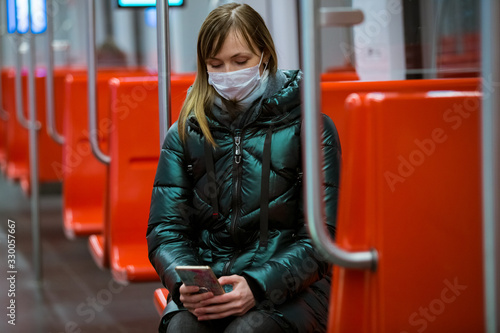 Woman in winter coat with protective mask on face sitting in subway car, using phone, looking worried. Preventive measures in public places of epidemic regions. Finland, Espoo