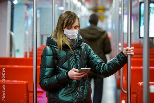 Woman in winter coat with protective mask on face standing in subway car, using phone, looking worried. Preventive measures in public places of epidemic regions. Finland, Espoo